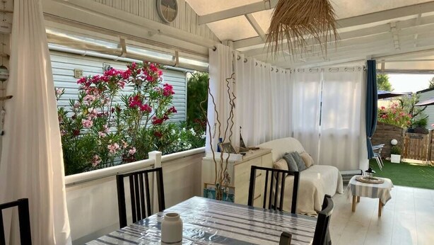 Eine überdachte Terrasse mit Esstisch, Stühlen, einer Couch und einer hängenden Leuchte.