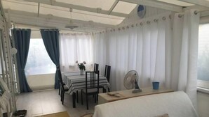 Ein Zimmer mit einem Bett, einem Esstisch mit Stühlen, einem Ventilator und Vorhängen.