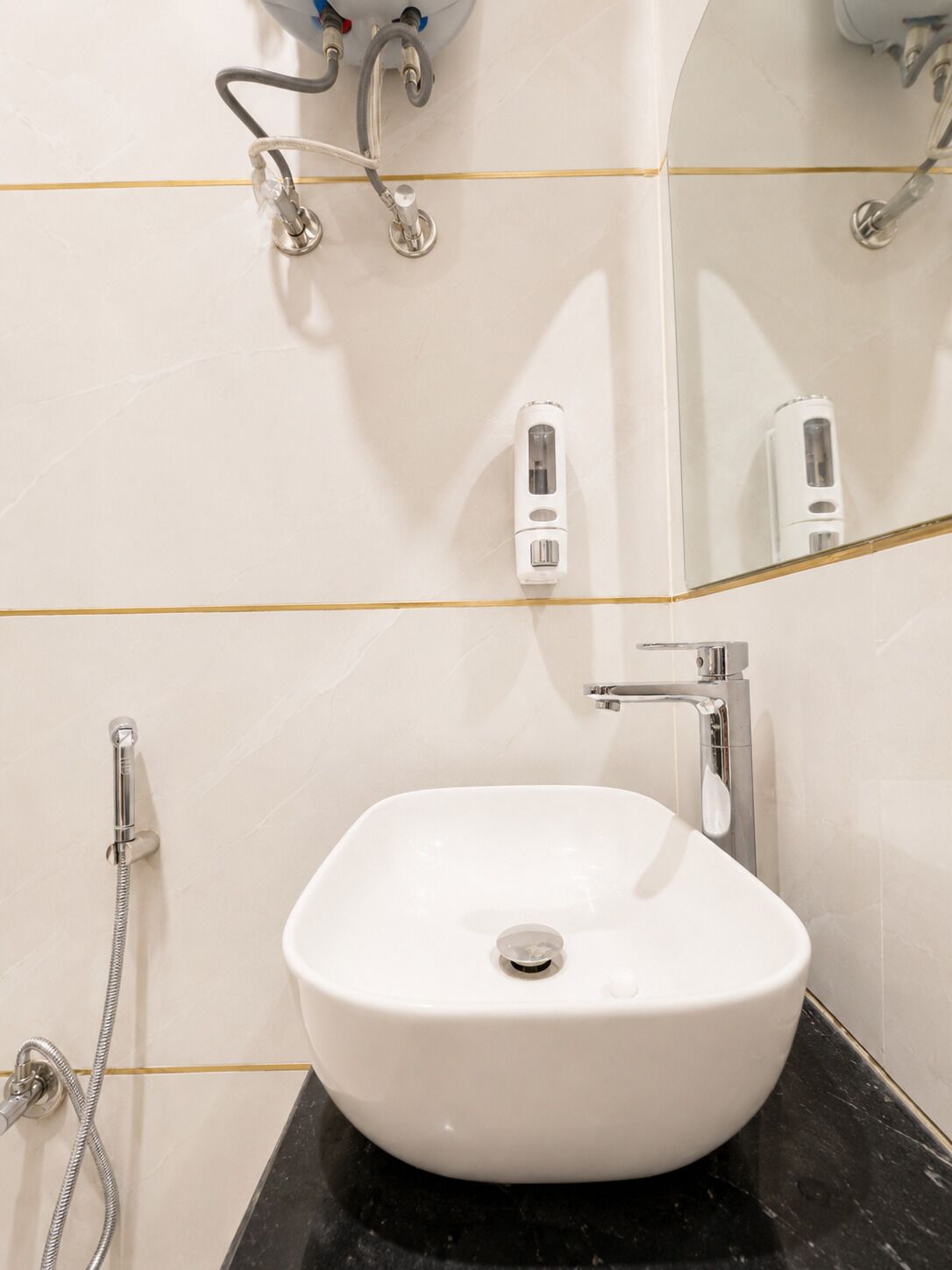 A bathroom with a white sink, a handheld showerhead, a mirror, and a wall-mounted soap dispenser.