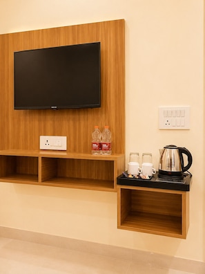 Una TV a muro, una presa di corrente, due bottiglie d'acqua, un bollitore e un vassoio con tazze e teiera.