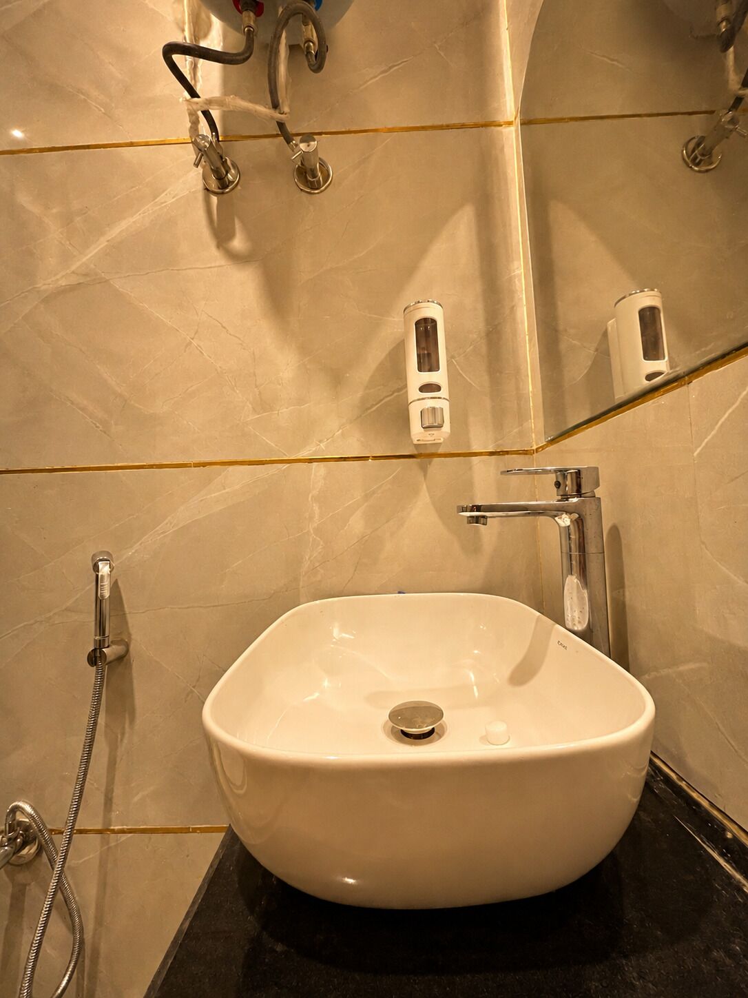 A bathroom with a white sink, a handheld showerhead, and a soap dispenser.