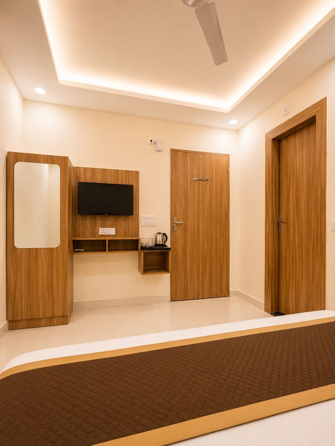 Moderni hotellihuone, jossa on taulutelevisio, puinen vaatekaappi ja pieni hylly, jonka päällä on vedenkeitin.