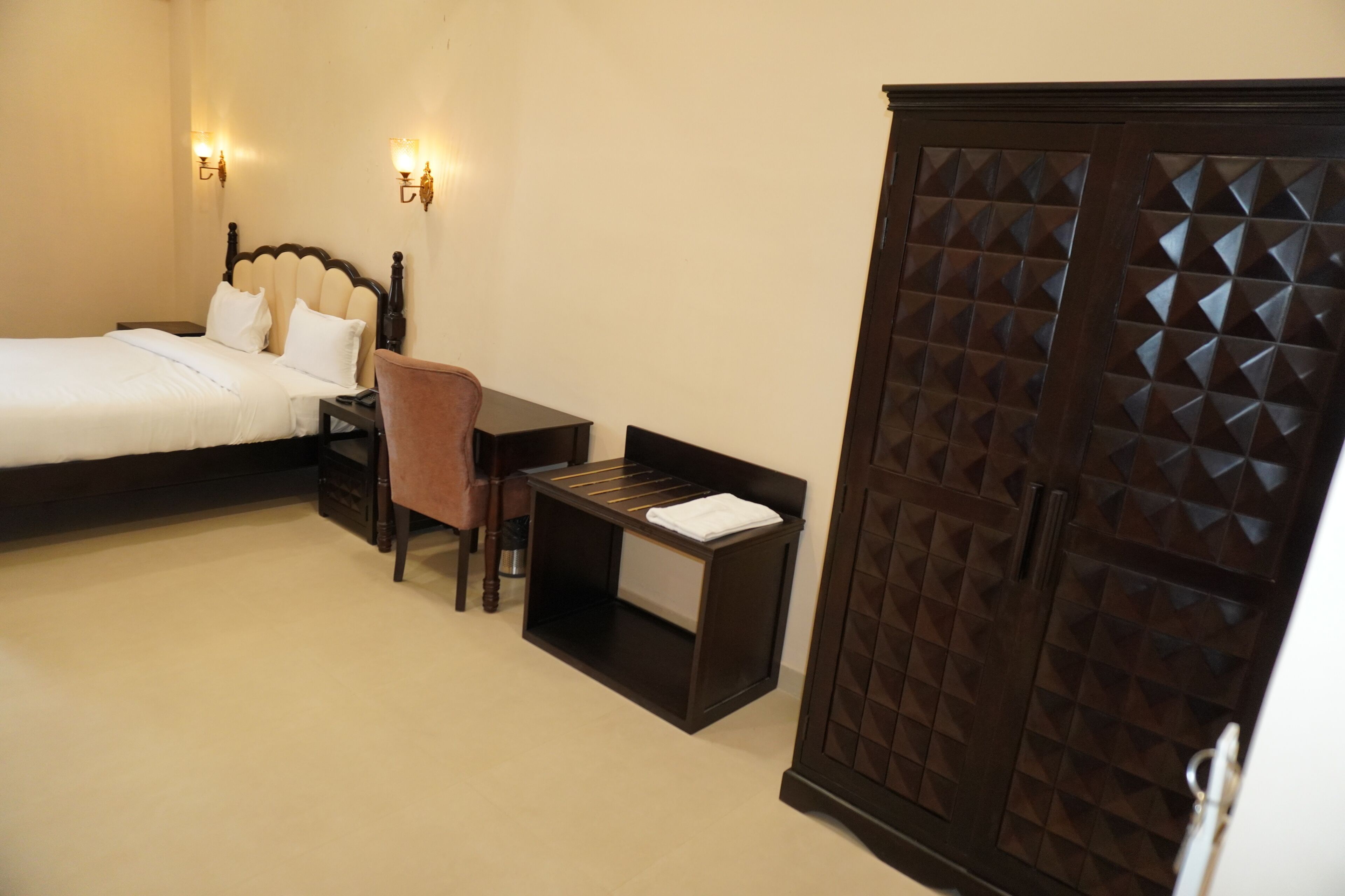 A bedroom with a bed, a desk, a chair, a wardrobe, and two wall-mounted lights.