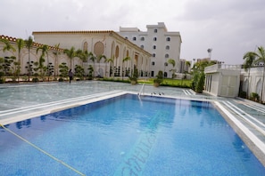 Una piscina con borde de azulejos, rodeada de palmeras y un edificio de arquitectura tradicional.