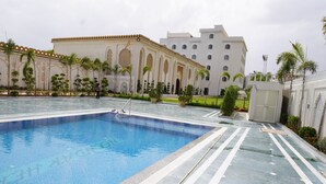 A swimming pool with a tiled deck, surrounded by a building with arched windows and a flagpole. - Neendar Heritage Resort (Jaipur)