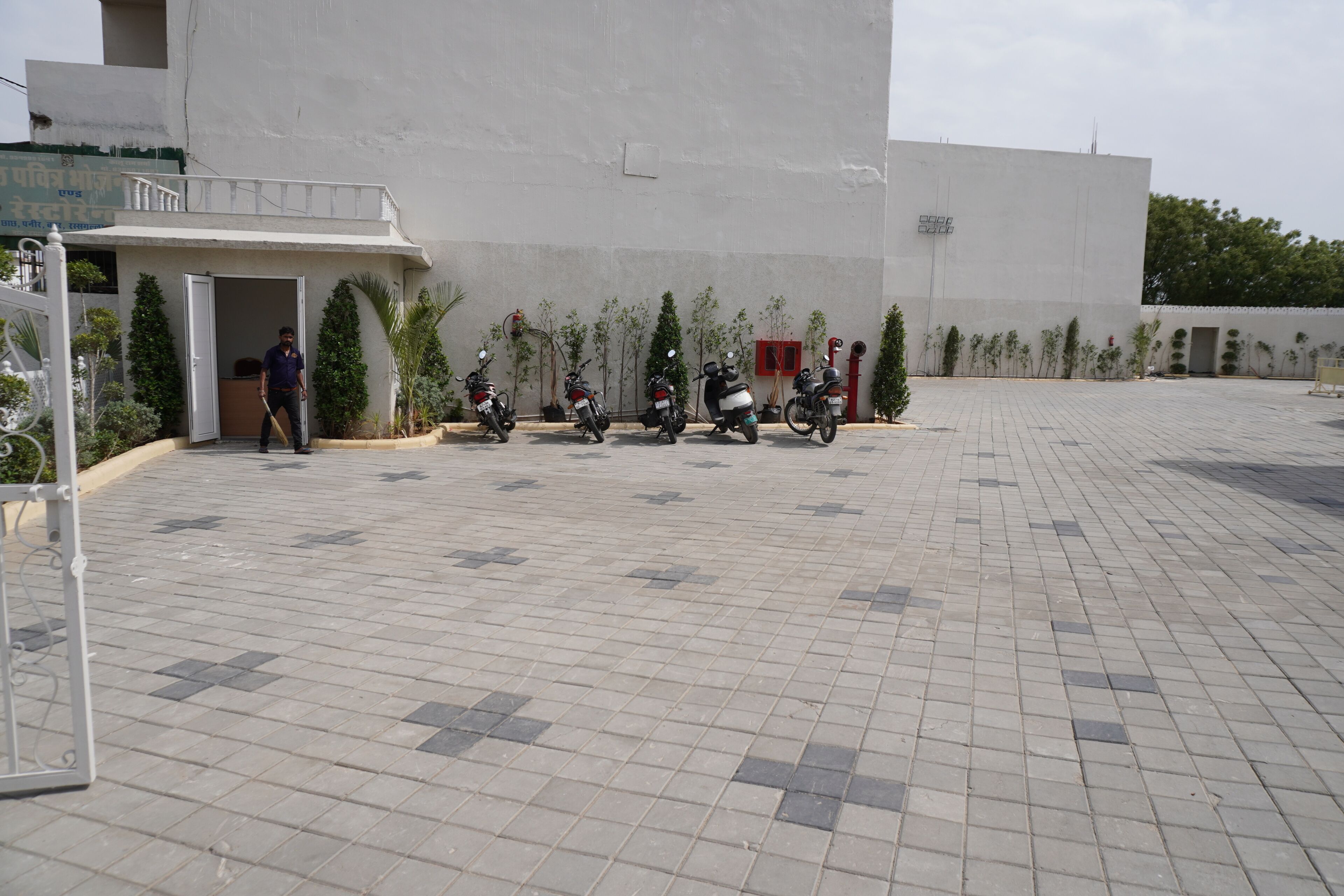 Un patio empedrado con entrada a un edificio, varias scooters estacionadas y macetas con plantas.