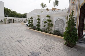 Un patio con suelo empedrado, un edificio blanco con arcos decorativos y un vehículo estacionado al fondo.