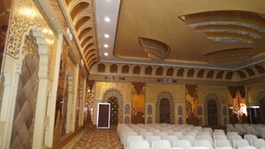 An indoor venue with rows of white chairs, ornate wall decorations, and a patterned carpet. - Neendar Heritage Resort (Jaipur)