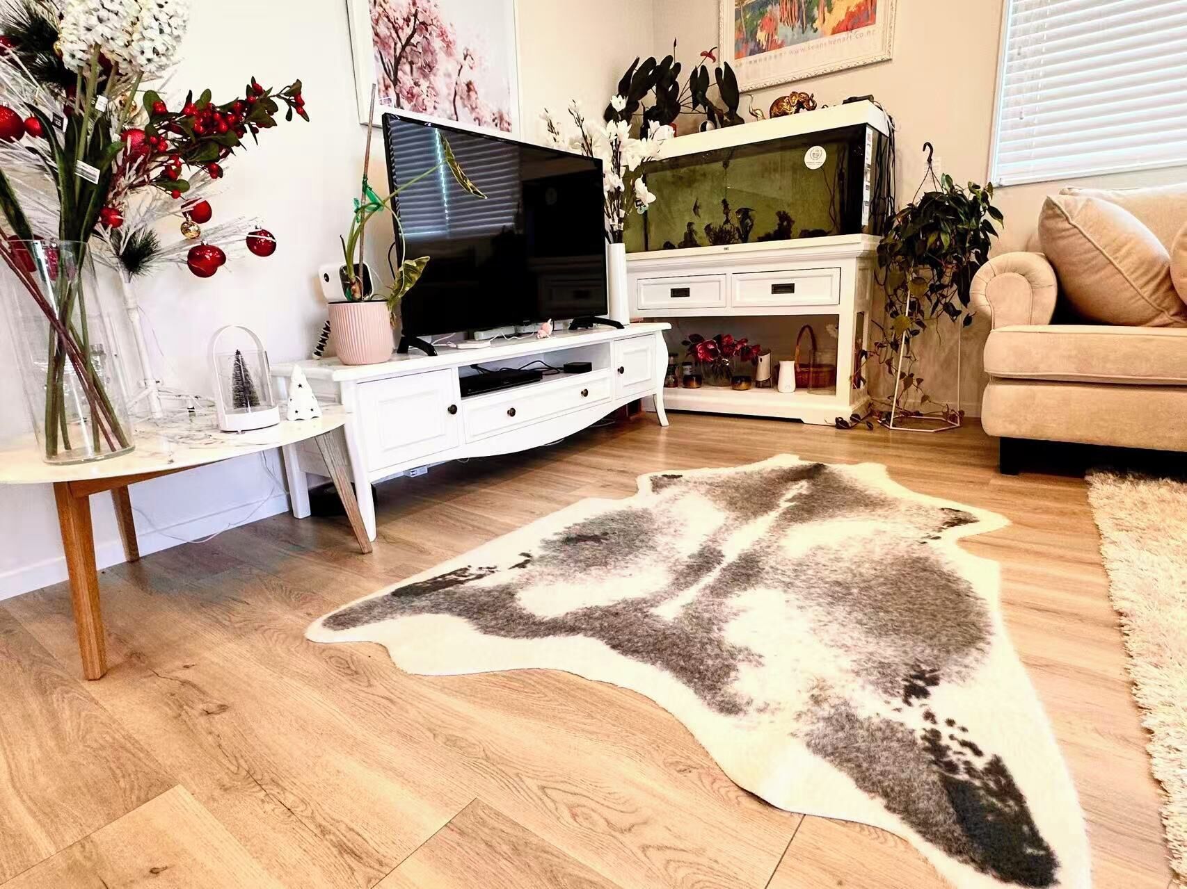 A living room with a flat-screen TV, white furniture, a large rug, and decorative plants.