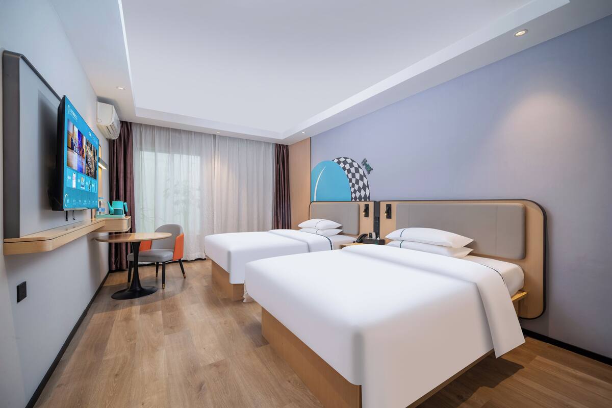 Quarto de hotel com duas camas, uma escrivaninha, uma cadeira, uma televisão e uma luminária.