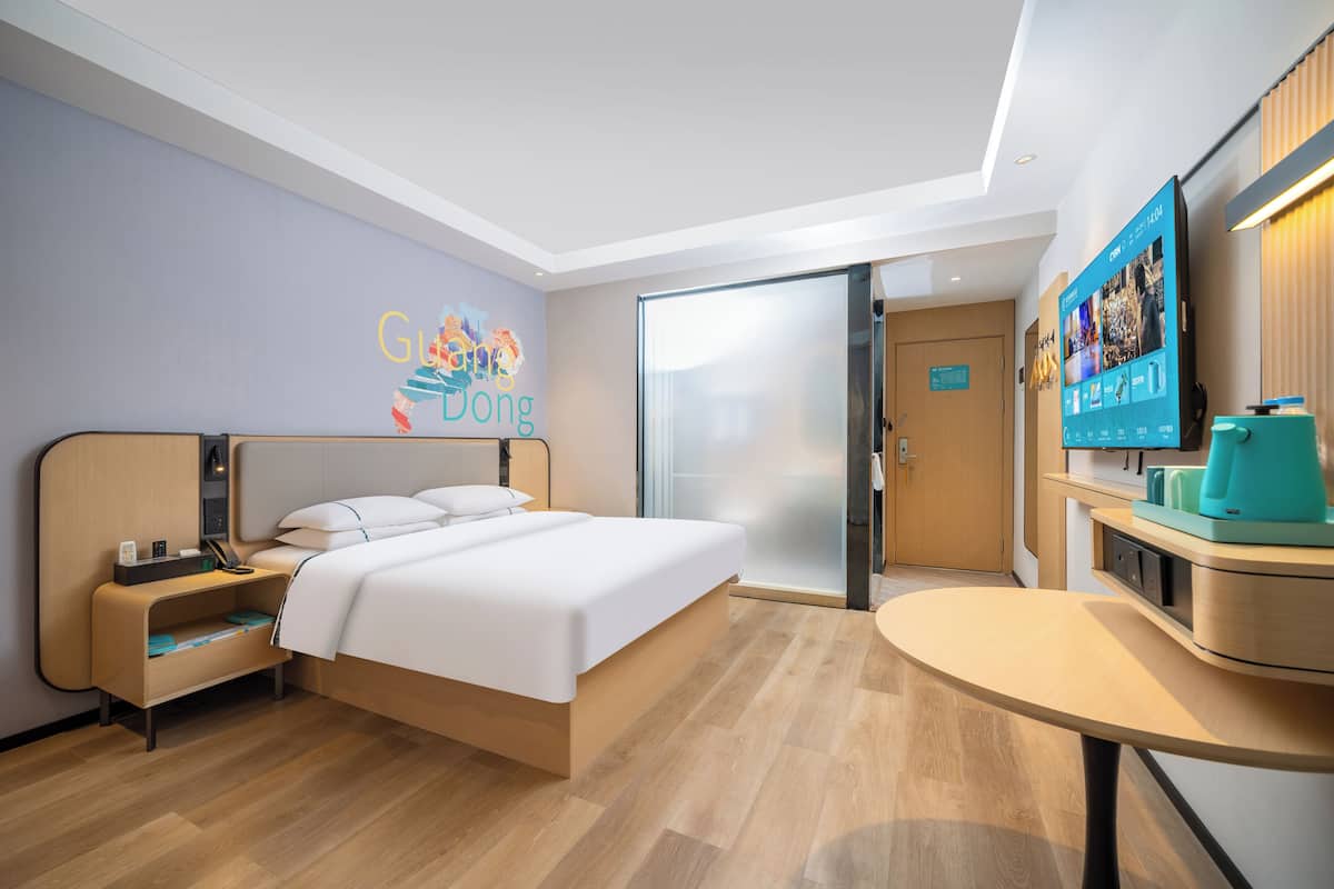 Quarto de hotel com cama, escrivaninha, televisão e porta deslizante.