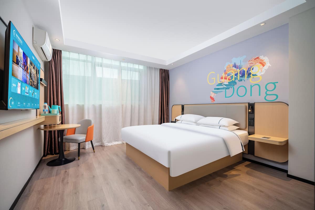 Quarto de hotel com cama, escrivaninha, cadeira, televisão e parede com mural da paisagem urbana.