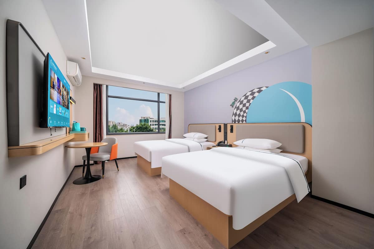 Quarto de hotel com duas camas, televisão, escrivaninha e janela com vista para a cidade.