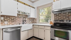 A kitchen with white cabinets, a brick backsplash, a stainless steel dishwasher, and an oven.