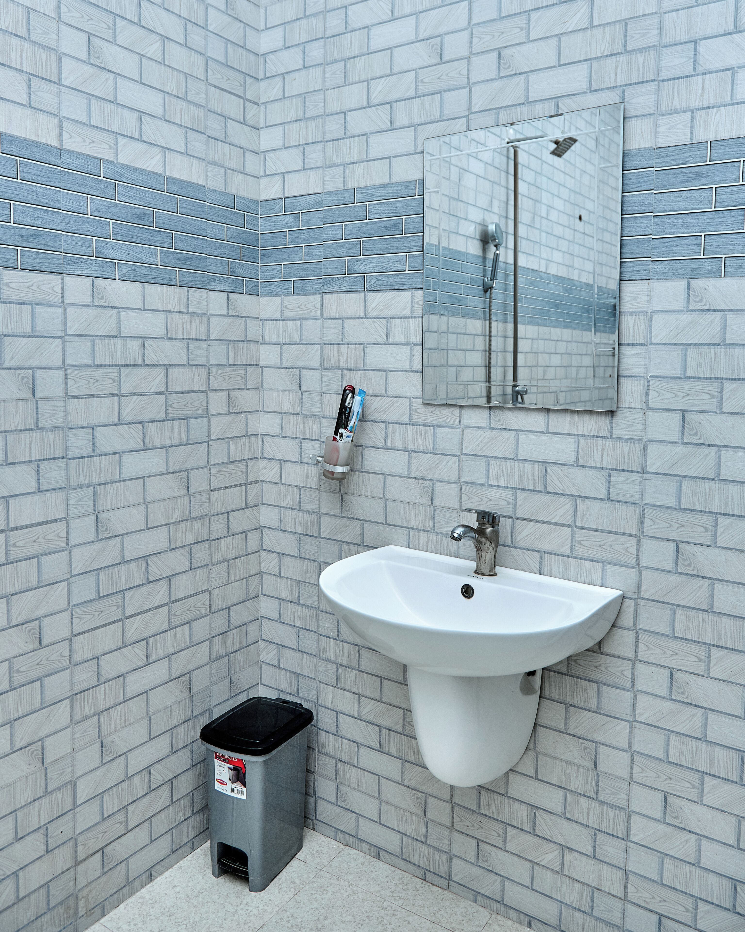 A bathroom with a white sink, a mirror, and a trash bin.