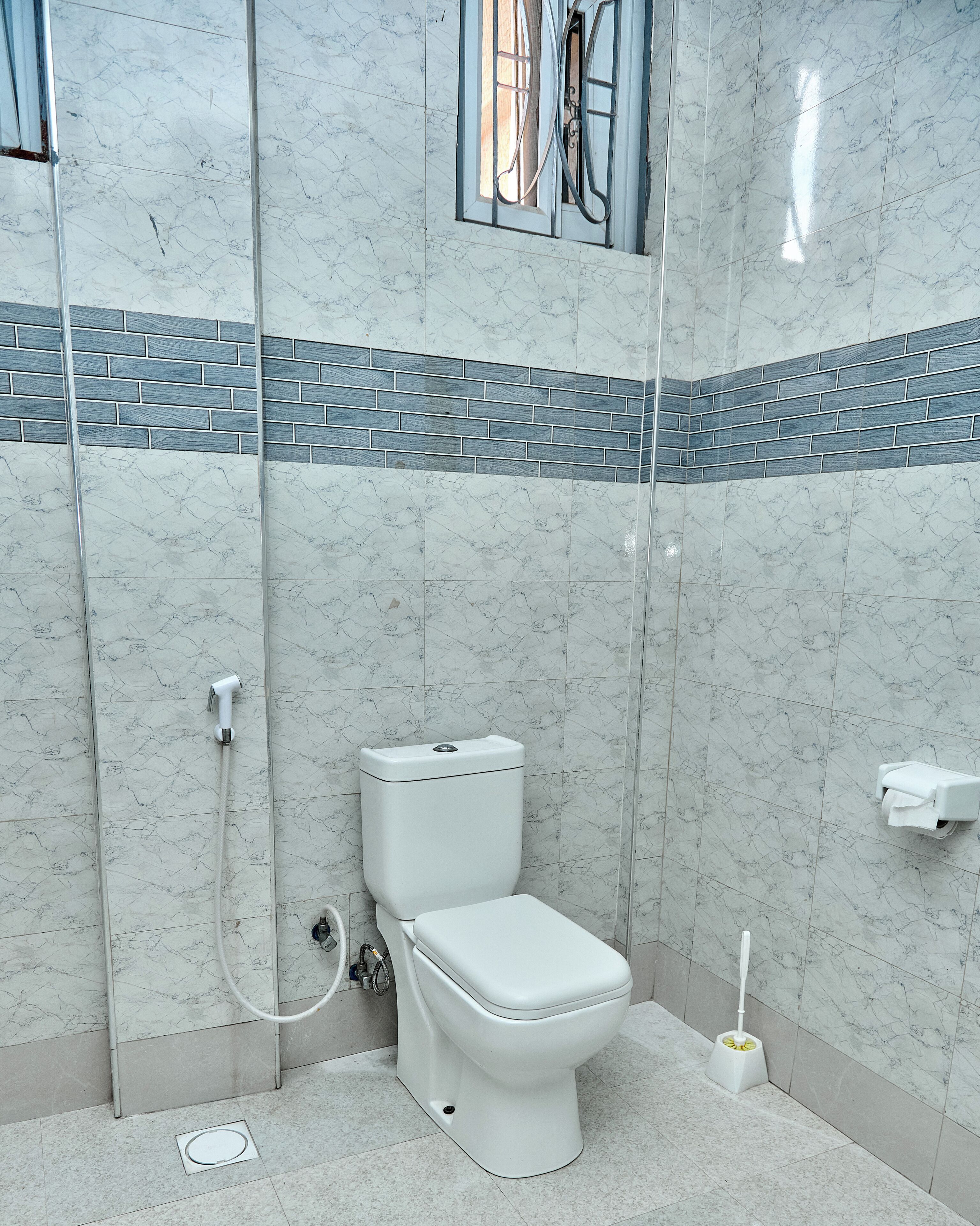 A bathroom with a toilet, shower, and a window.