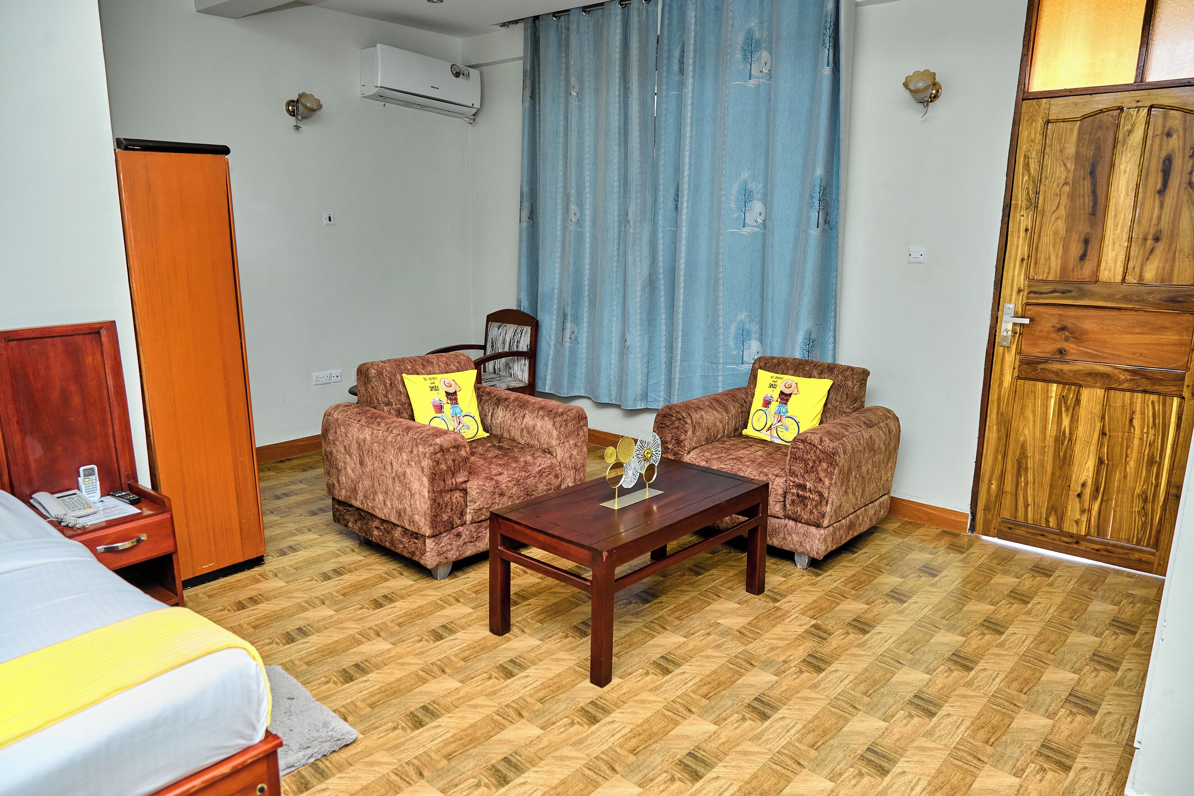 A room with a bed, two sofas, a coffee table, a wooden door, and a window with curtains.