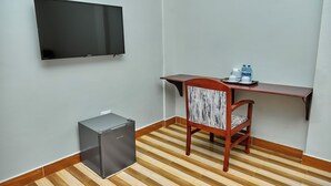 Une petite pièce équipée d’un téléviseur à écran plat fixé au mur, d’un bureau en bois avec une chaise et d’un petit réfrigérateur.