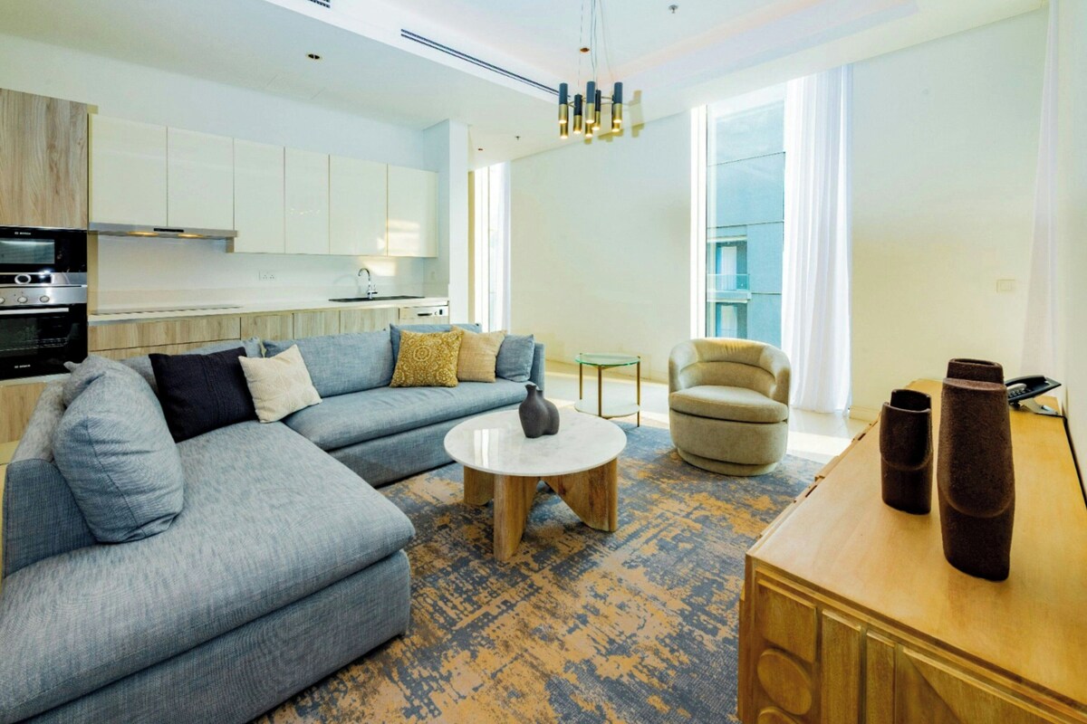 A modern living room with a sectional sofa, a round coffee table, a small side table, and a wooden console table with vases.