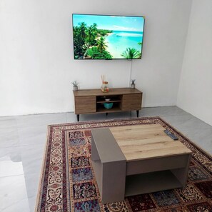Uma sala de estar moderna com uma televisão de tela plana, uma mesa de centro de madeira, um tapete estampado e um armário minimalista.