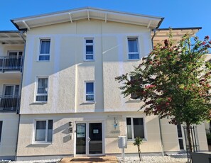 A multi-story building with a flat facade, multiple windows, and a door with signage. - Central but quiet, balcony, free swimming pool and sauna - Villa Elisenhof Elli 5 (Göhren (Ostseebad))