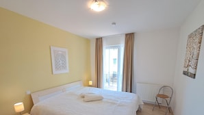 Een slaapkamer met een bed, nachtkastje, lamp en uitzicht.