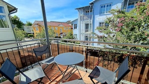 Een balkon met een tafel en stoelen, een hekwerk en uitzicht op omliggende gebouwen.