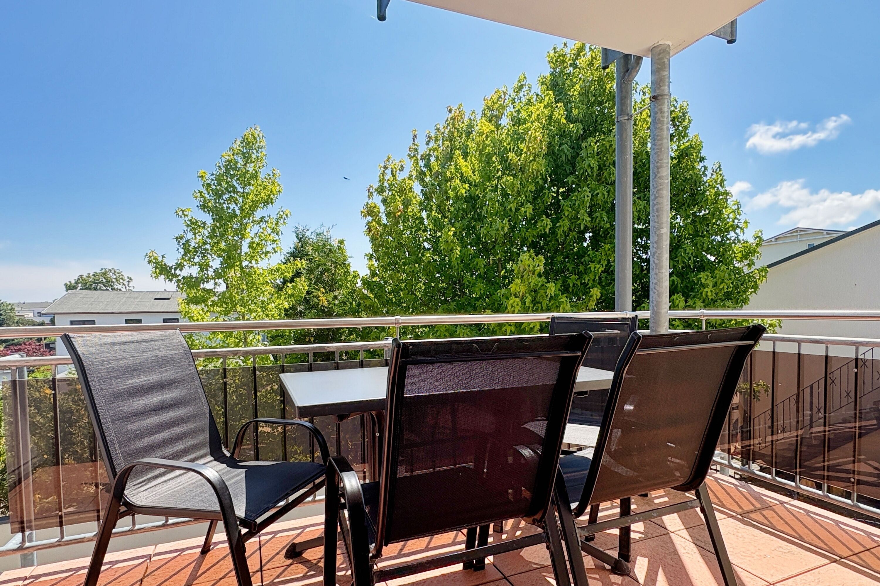 A balcony with a table and chairs, a railing, and a view of trees and buildings.