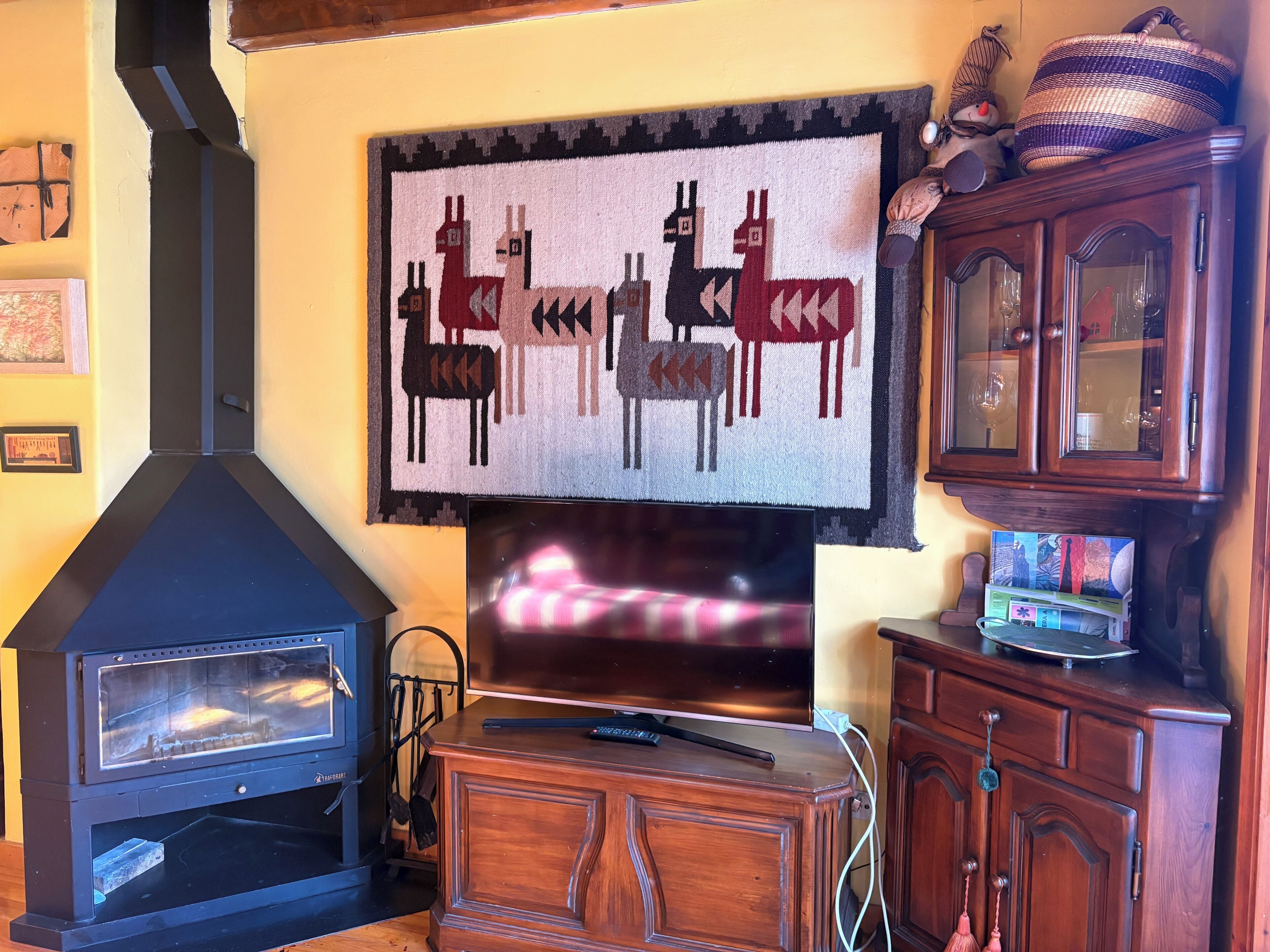 Ein Wohnzimmer mit Kamin, Fernseher, einer Holzkommode und einem Teppich mit Tiermotiven.
