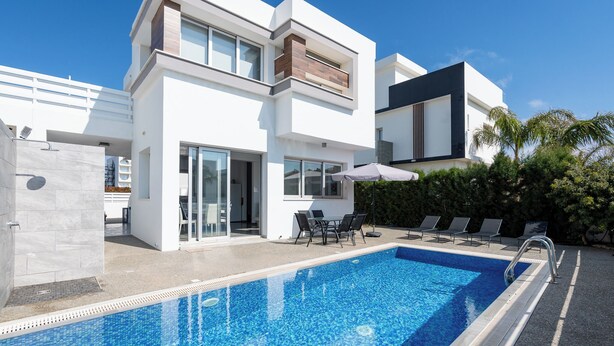 Ein modernes, zweistöckiges Haus mit Pool, Sitzgelegenheiten im Freien und einer überdachten Terrasse.