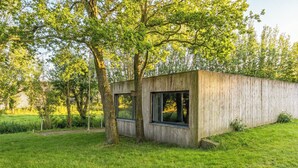 Una cabaña moderna de madera con ventanas amplias, rodeada de abundante follaje y árboles.