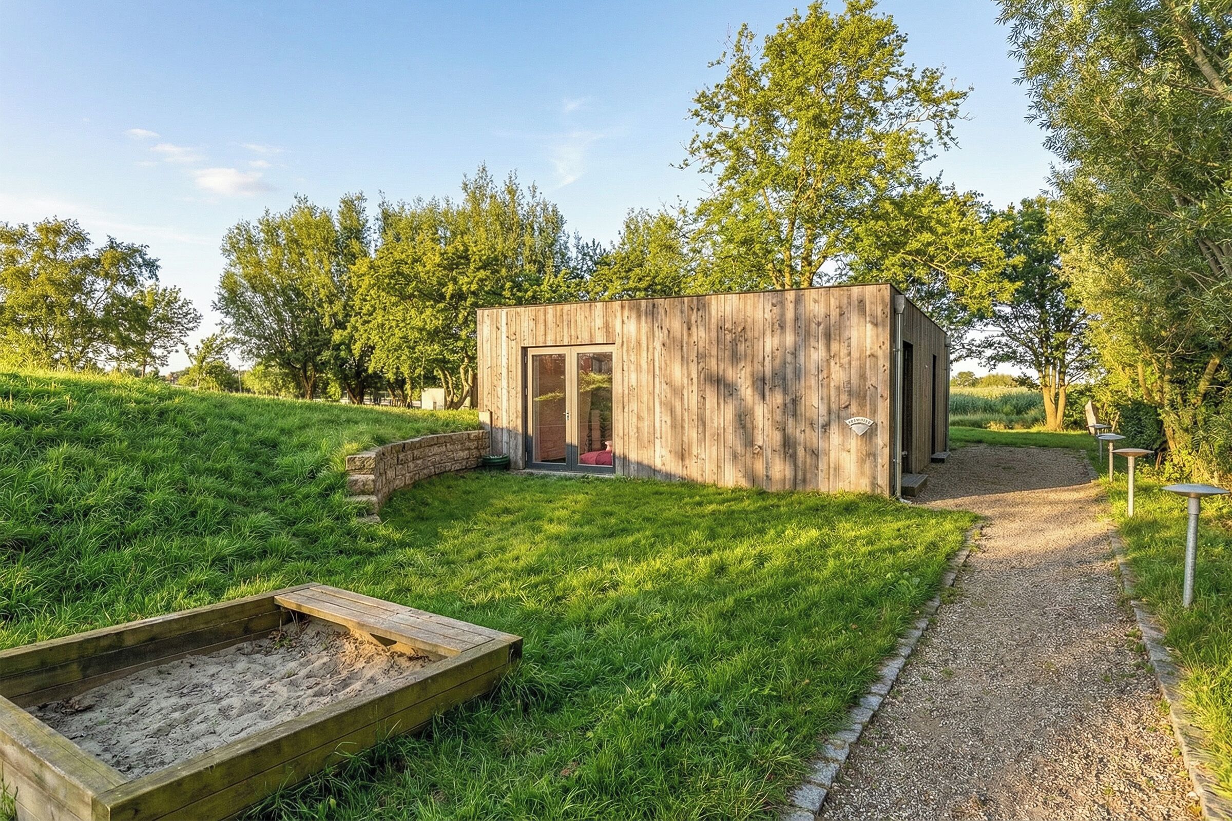 A wooden cabin with a gravel path leading to it, surrounded by grass and trees.