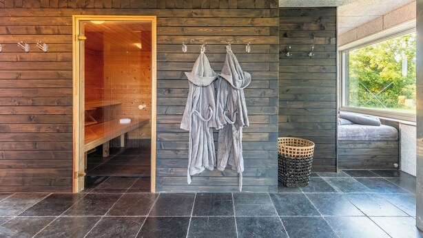 Un moderno spa con una pared de madera, una puerta de vidrio que da a una sauna y una zona de estar con vistas a la vegetación.
