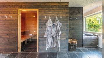 Une salle de spa moderne avec un mur en bois, une porte en verre donnant sur un sauna et un coin salon avec vue sur la verdure.