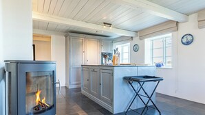 Una cocina moderna con estufa de leña, una isla central y un comedor con mesa.