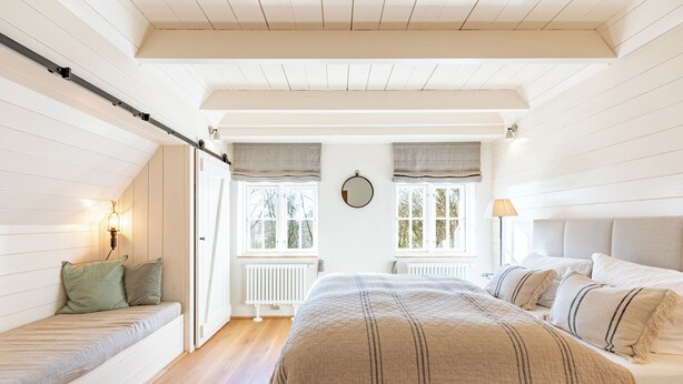 Una camera da letto con un letto, una panca, un termosifone e una finestra con tende.