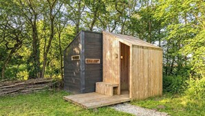 Una piccola baita di legno con veranda, immersa tra gli alberi.