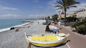 Ein Strand mit Booten, einer Palme und Gebäuden im Hintergrund.