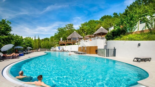 Ein Schwimmbecken mit Liegestühlen und Sonnenschirmen, umgeben von Gebäuden und Grünflächen.