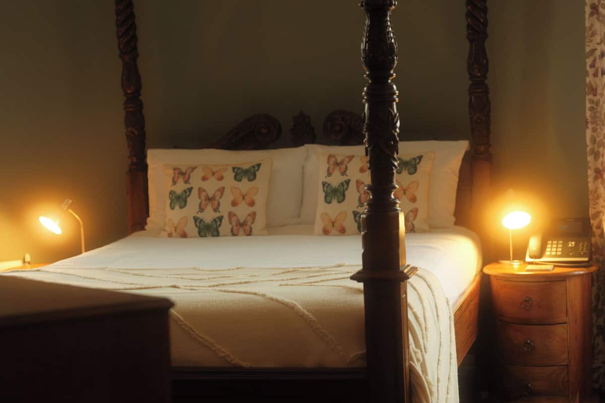 Ein Himmelbett mit einem floralen Kopfkissen, Nachttische mit Lampen und ein Beistelltischchen mit einem Telefon.