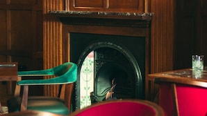 Une pièce aux murs lambrés, avec une cheminée et deux fauteuils dotés de coussins rouges.