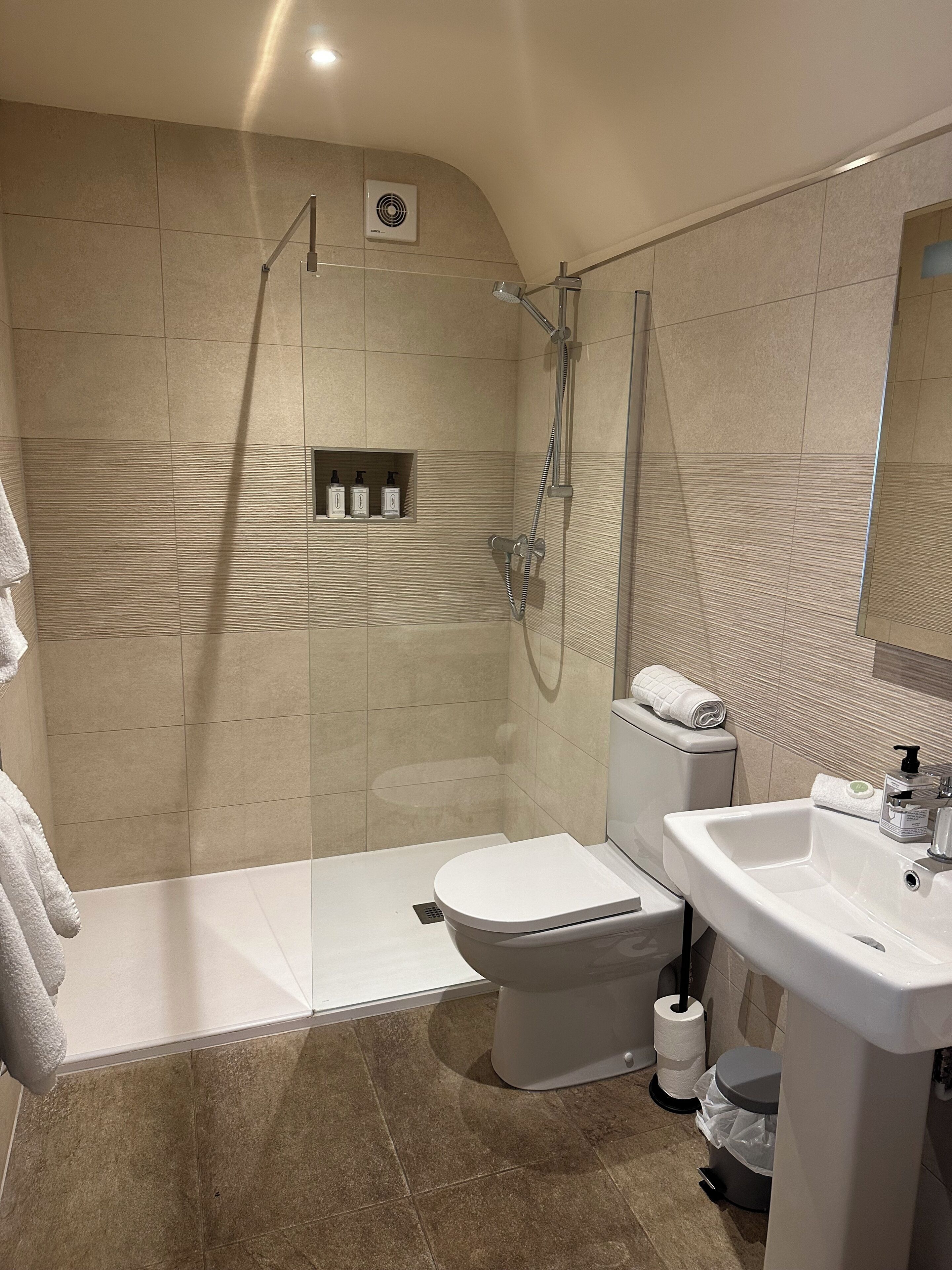 Un baño moderno con ducha, inodoro, lavabo y un pequeño estante con artículos de aseo.