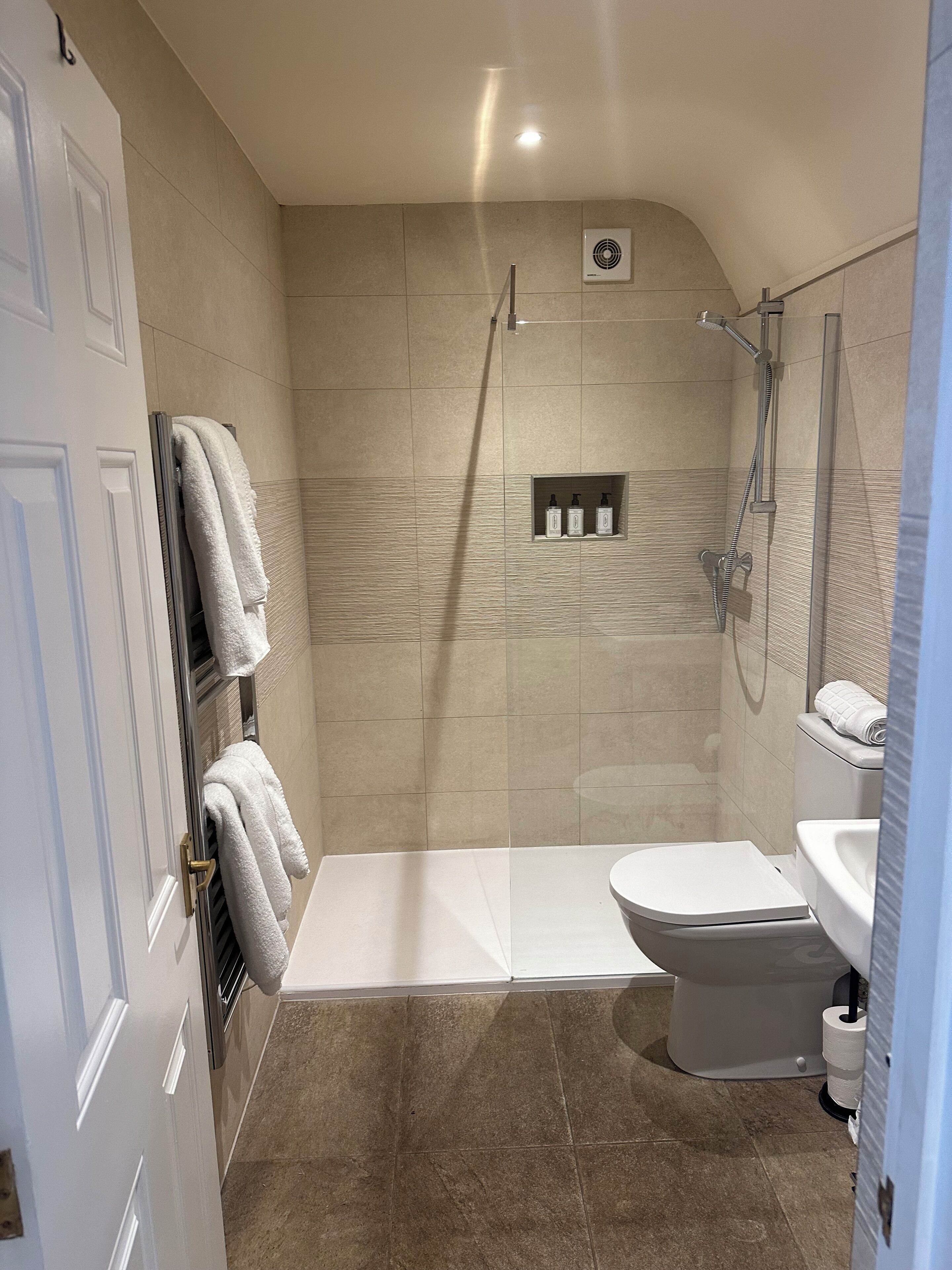 A modern bathroom with a shower, toilet, and sink, featuring beige tiles and a towel rack.