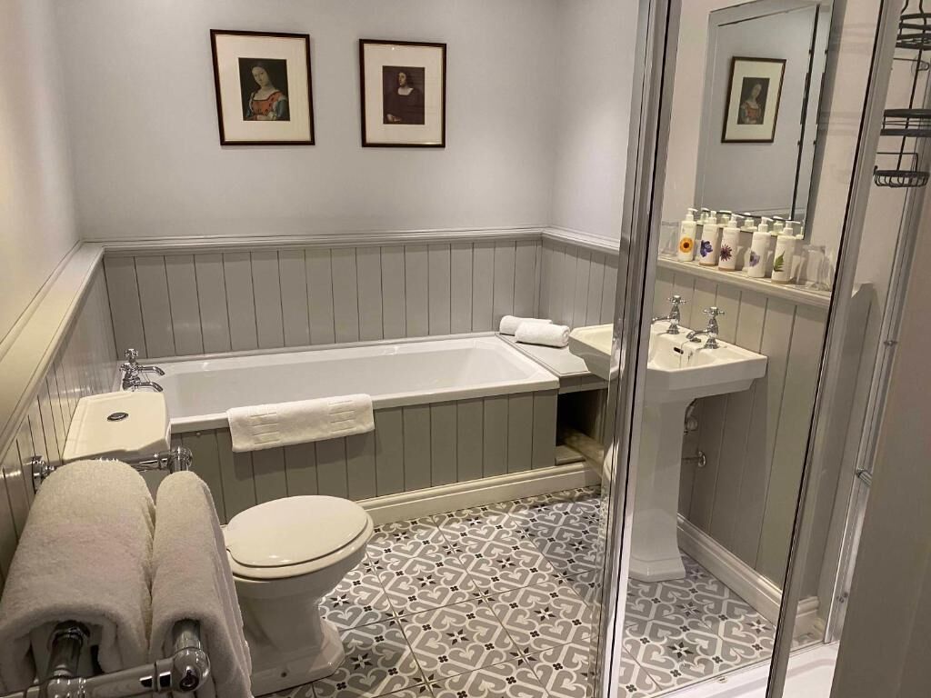Une salle de bain équipée d’une baignoire, de toilettes, d’un lavabo et d’une douche. Des tableaux encadrés ornent le mur.