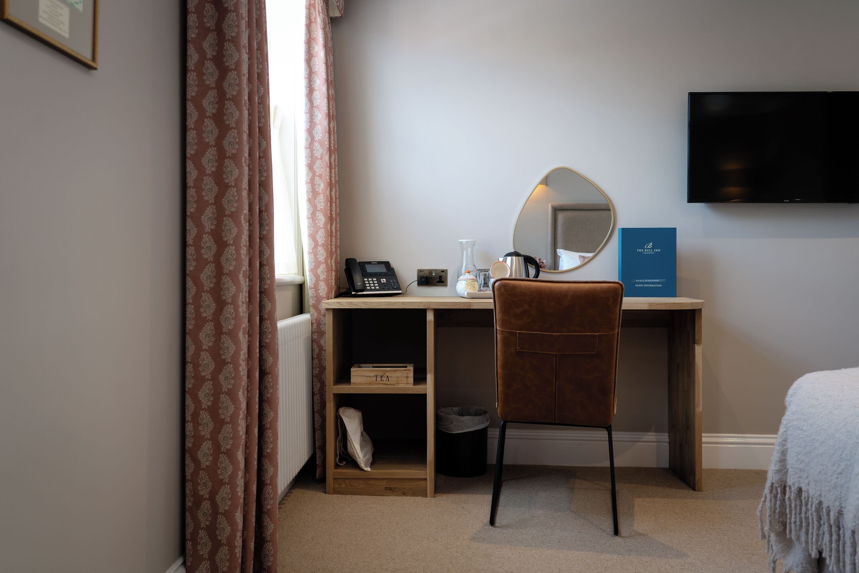 A hotel room with a desk, chair, TV, and a bed.
