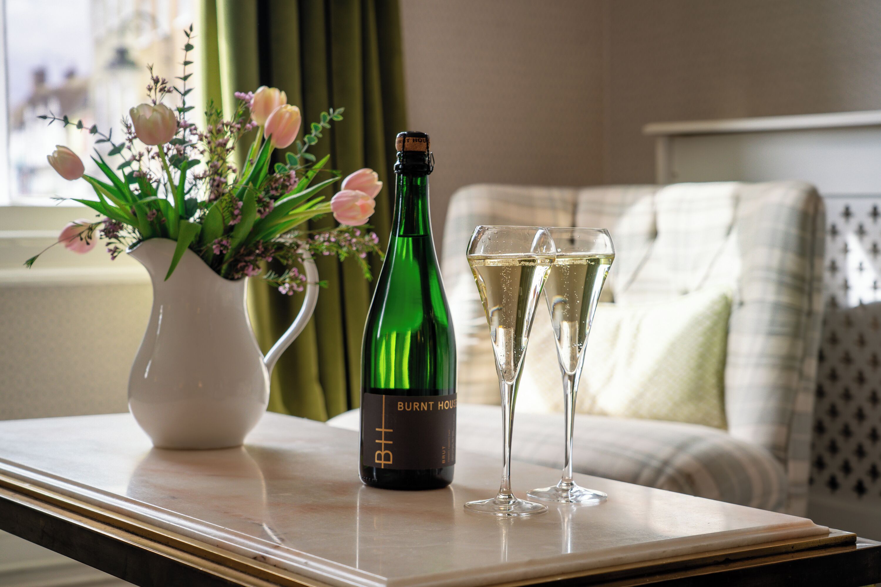 A bottle of wine and two glasses on a table with a vase of flowers.