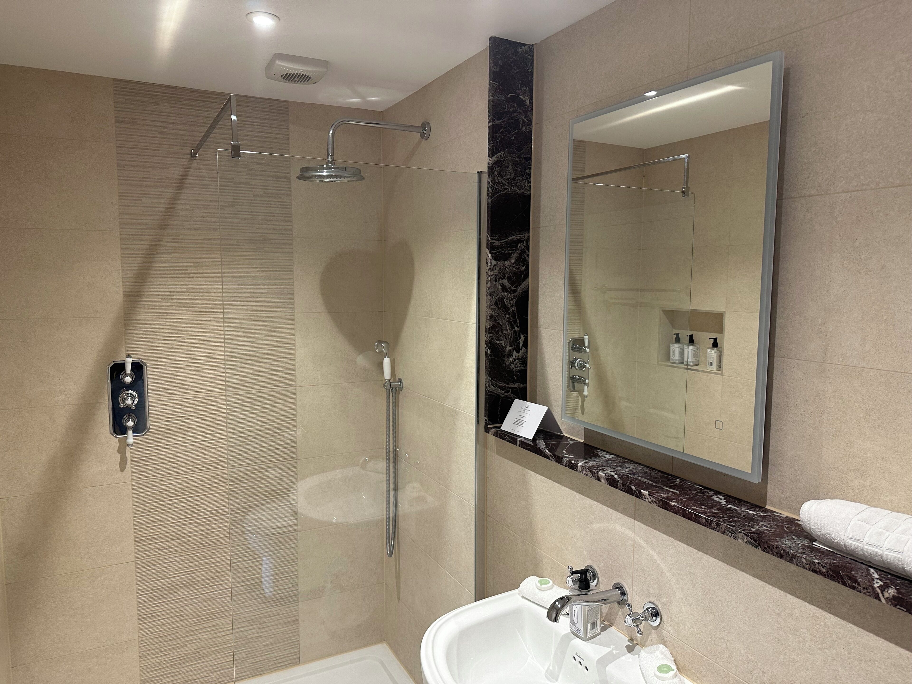 Une salle de bain moderne dotée d’une douche à parois de verre, d’un grand miroir et d’un lavabo avec un plan de travail en marbre.