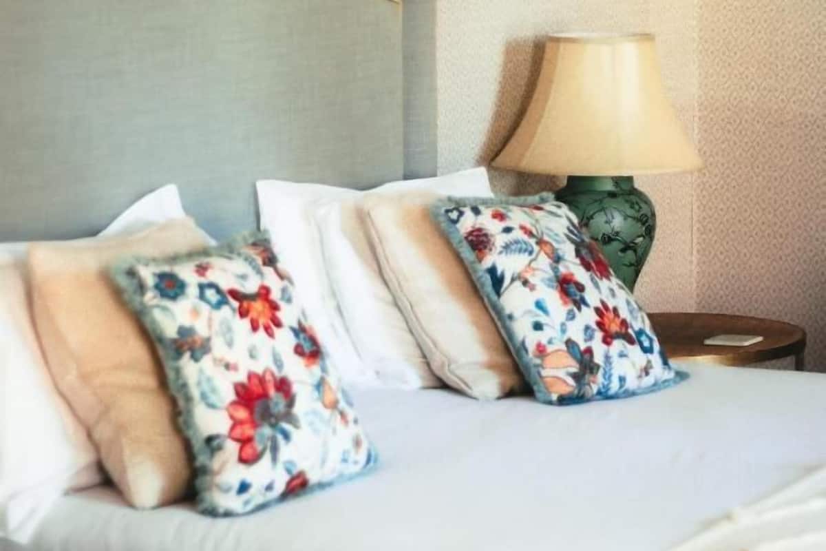 Ein Bett mit blumigen Kissen, einer grünen Lampe und einer strukturierten Wand.