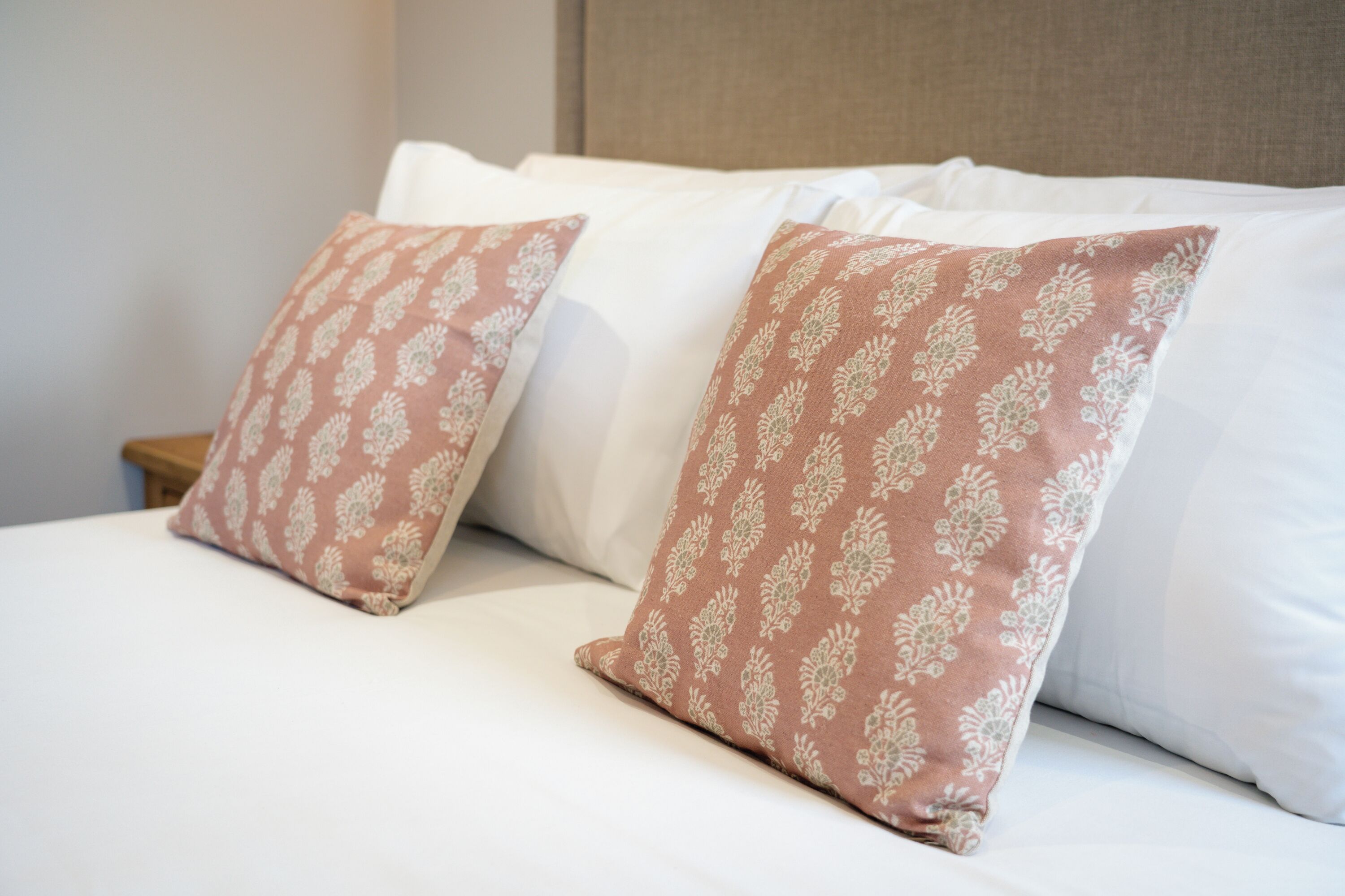 Una cama con almohadas blancas y estampadas, una mesita de noche de madera y un cabecero.