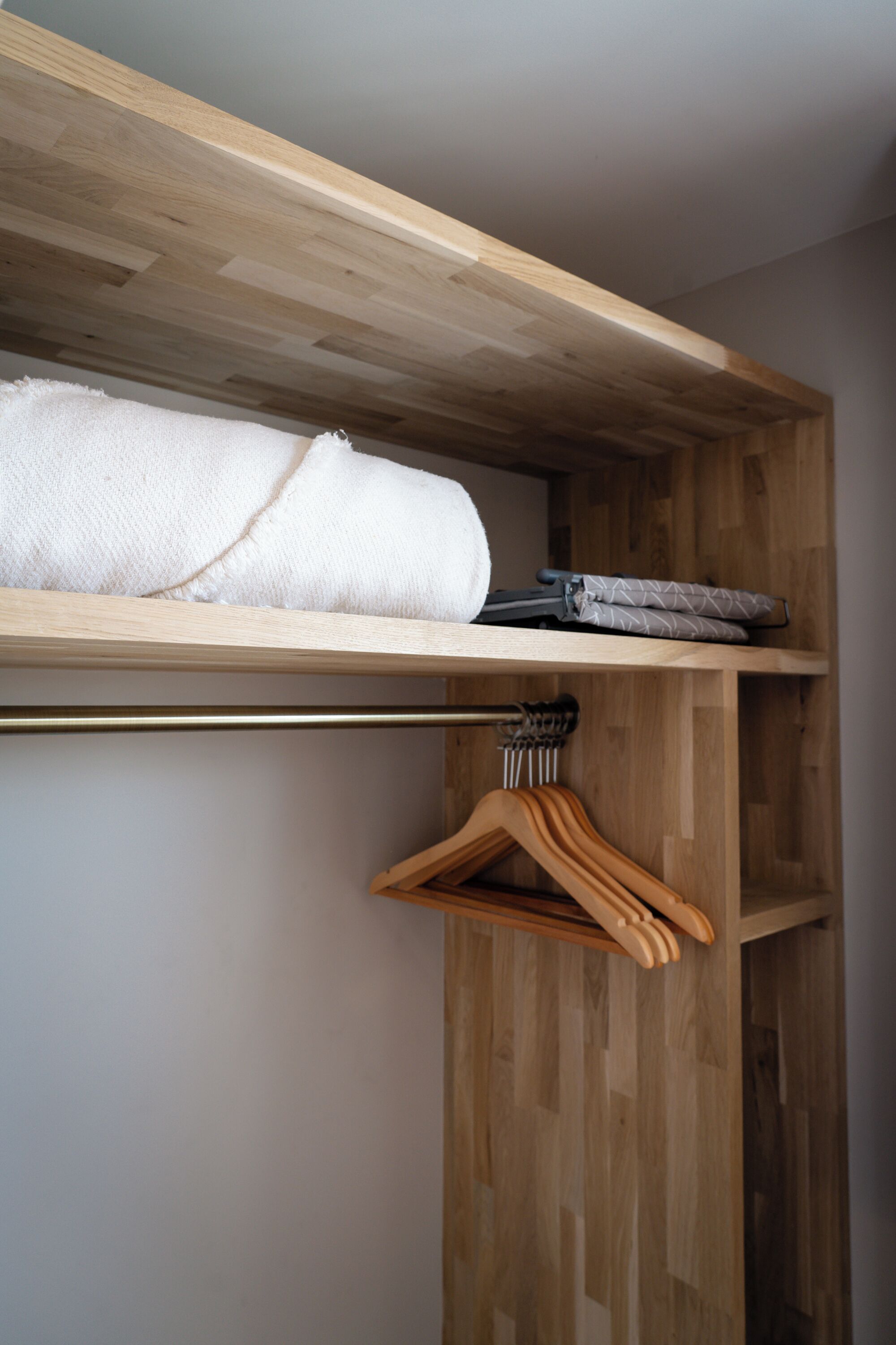 A wooden closet with a towel and folded clothes on the top shelf.